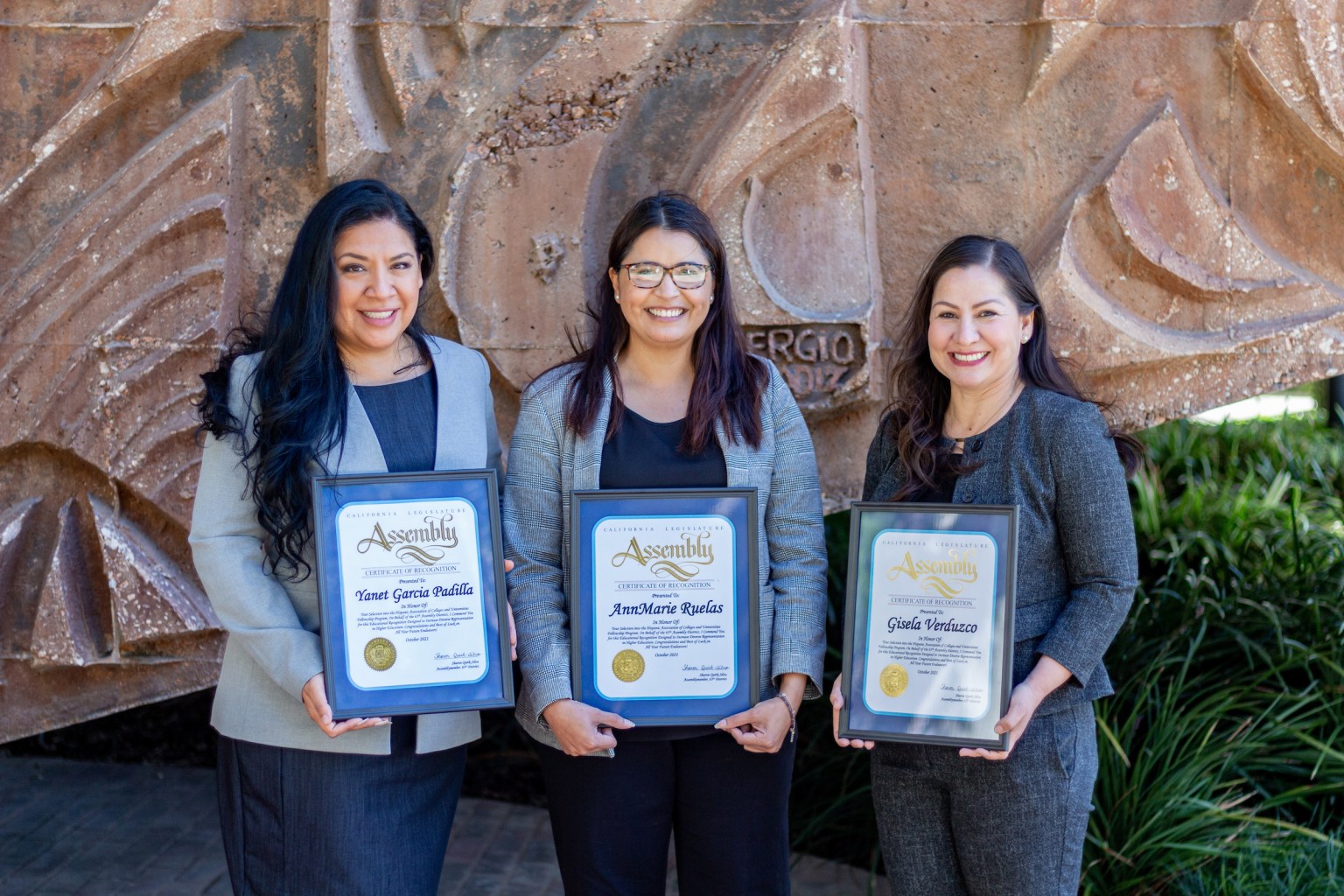 Three women standing in front of mural, holding awards