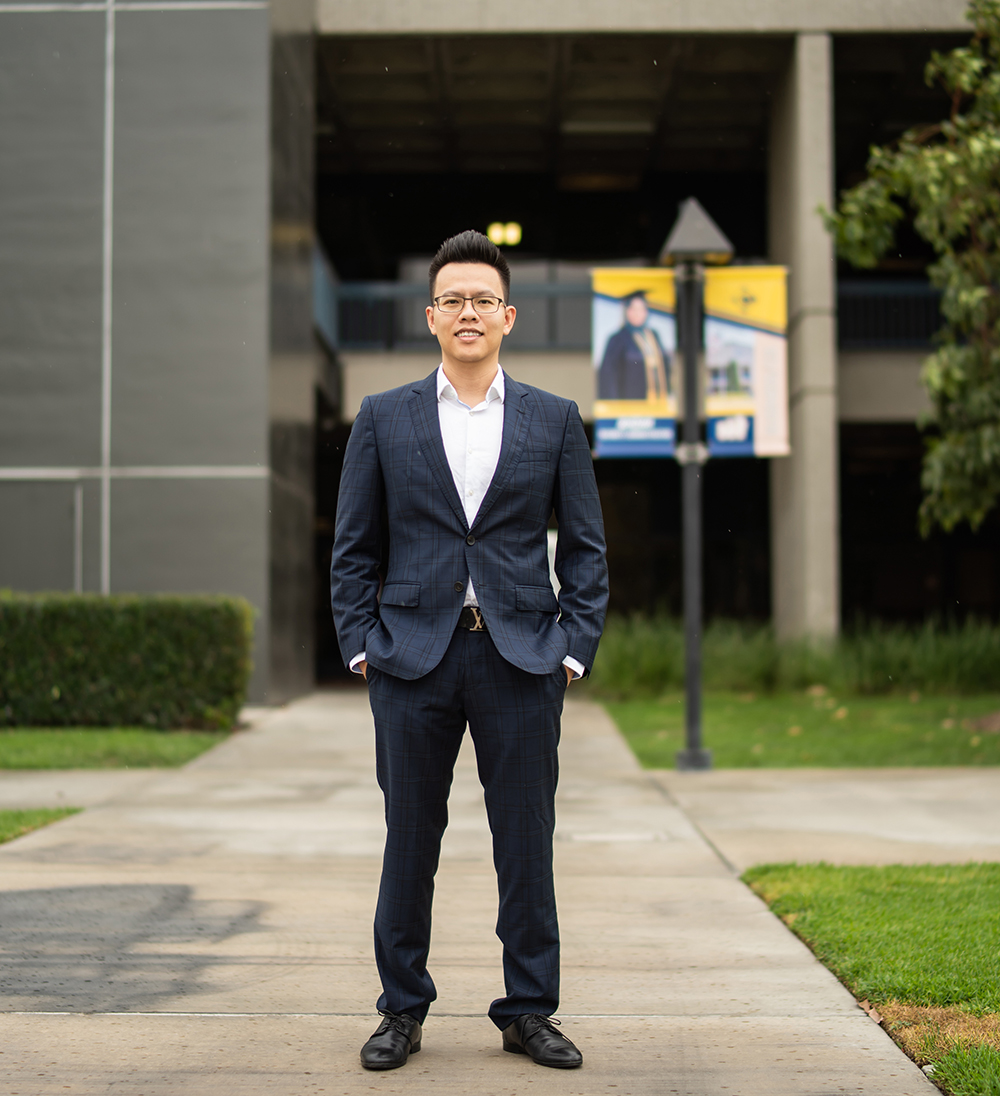 A man in a suit with his collar open stands in front of a breezeway by the Cypress College Business Education building.