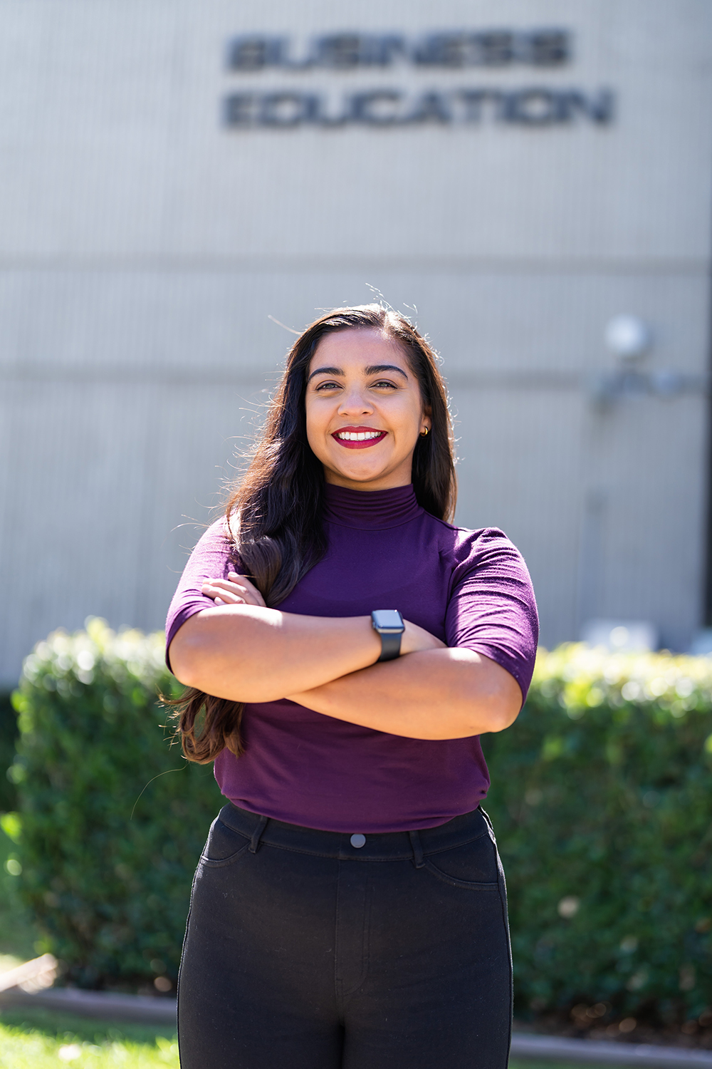 A woman smiles as she folds her arms and stands in front of the Business Education building on the campus of Cypress College.