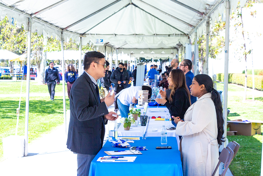 A student in professional attire speaks to a company representative at an information table on campus.