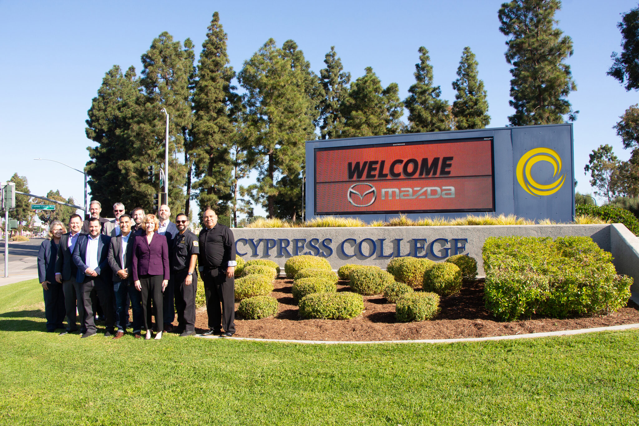 Members of Mazda North America Operations and the president, vice president of instruction, and faculty from Cypress College pose in front of the campus sign and digital marquee. 